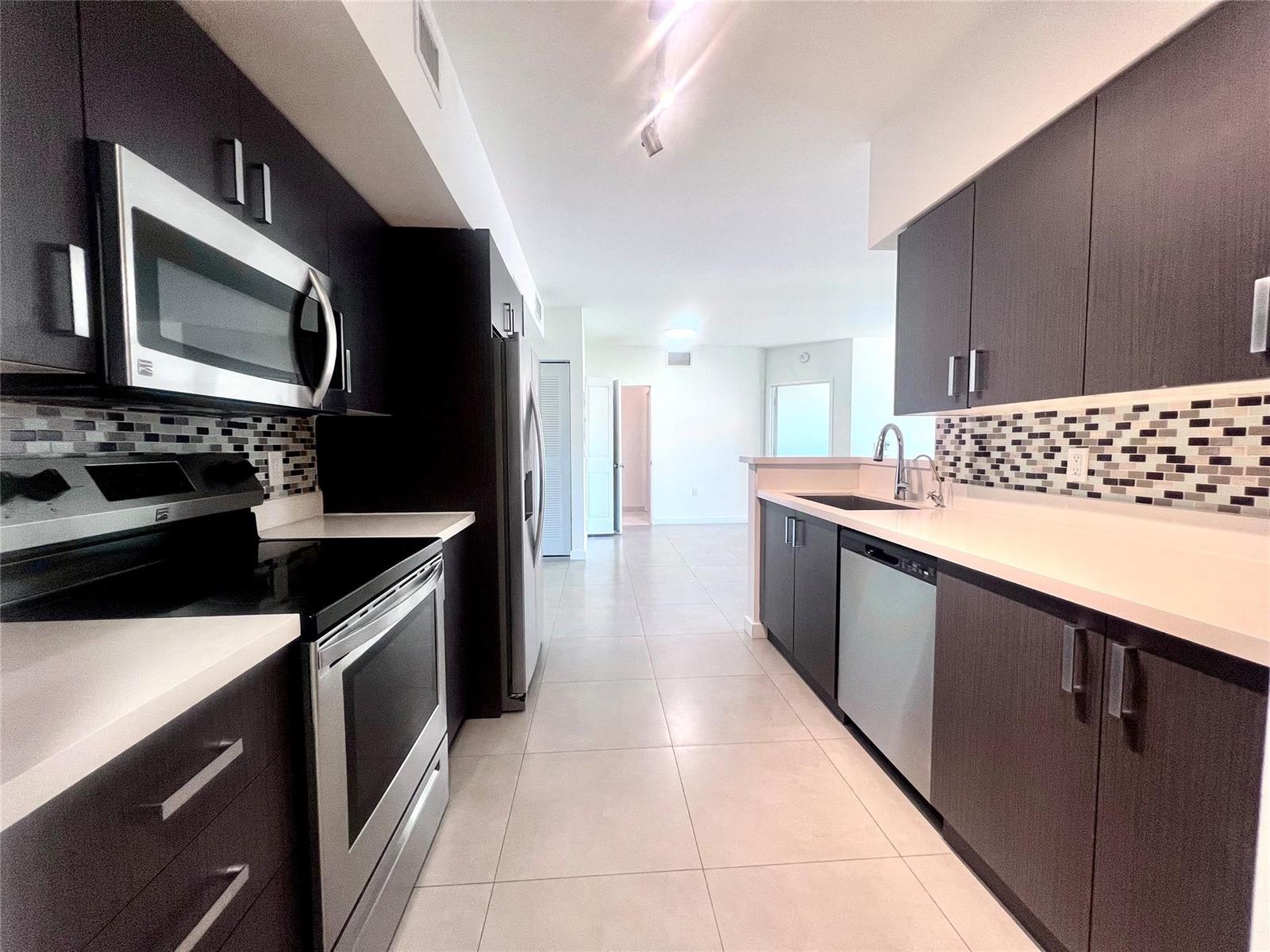 A modern galley kitchen features dark wood cabinets, stainless steel appliances, and white countertops — 729 NW 2 Street # 501, Miami FL 33128, MIAMI, FL