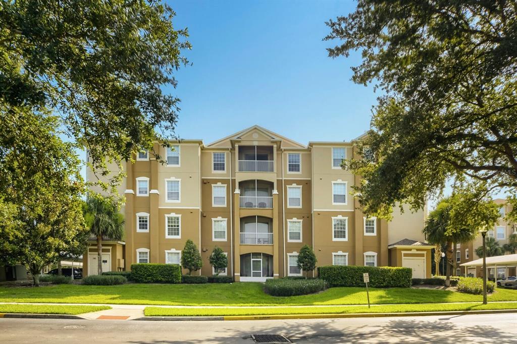 A multi-story apartment building with tan stucco walls, white trim, and screened balconies — 6466 CAVA ALTA DRIVE UNIT 208, ORLANDO, FL