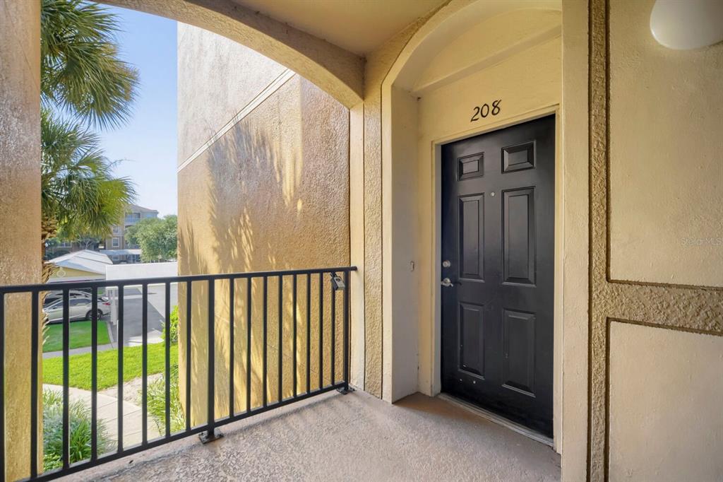 A black front door labeled 208 is located on a covered balcony with metal railings — 6466 CAVA ALTA DRIVE UNIT 208, ORLANDO, FL