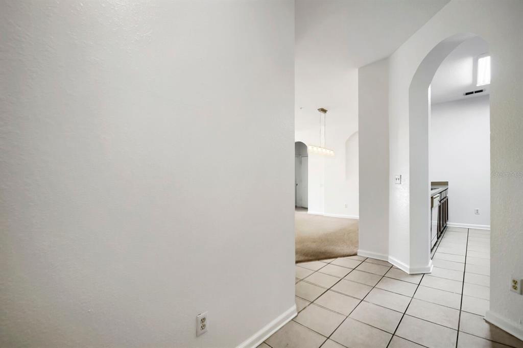 A hallway with white walls and tiled flooring leads toward an arched entryway — 6466 CAVA ALTA DRIVE UNIT 208, ORLANDO, FL