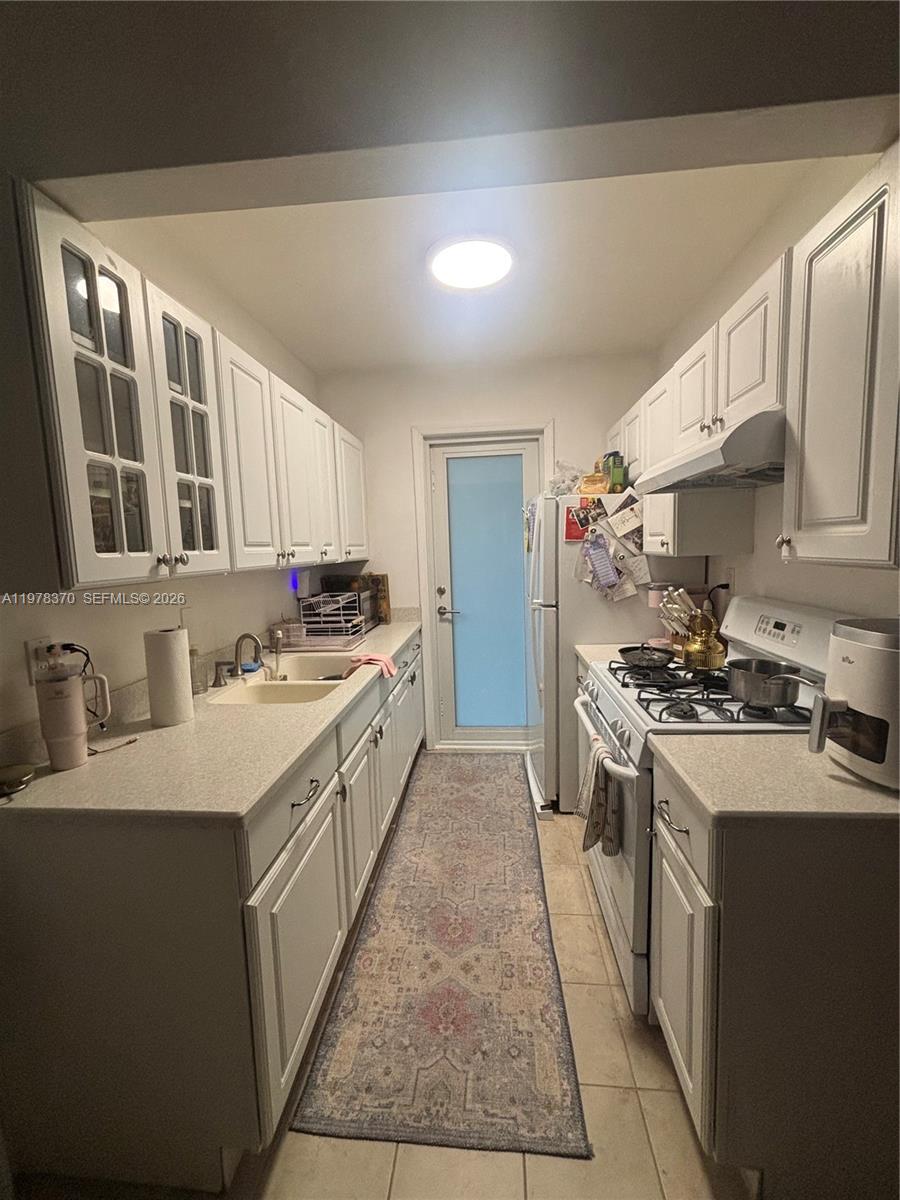 A narrow galley kitchen features white cabinets, light countertops, and a long patterned runner rug — 75 Washington Ave # 12A, Miami Beach FL 33139, MIAMI BEACH, FL