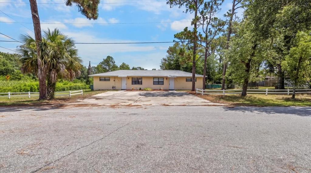 A single-story duplex with a concrete driveway sits behind a white fence under trees — 3135 S LANTANA WAY, HOMOSASSA, FL
