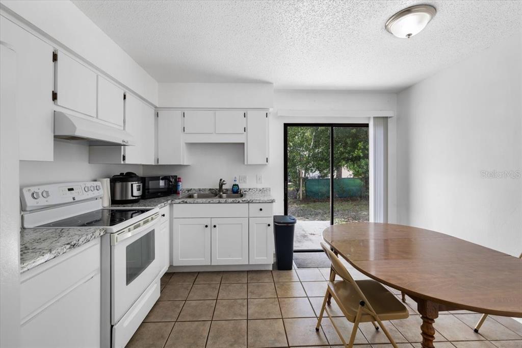 A kitchen with white cabinets, granite countertops, and a dining area with a sliding door — 3135 S LANTANA WAY, HOMOSASSA, FL