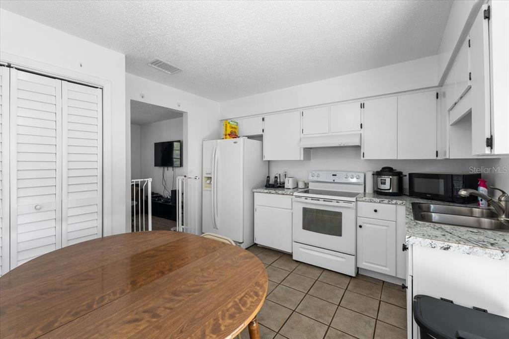 A kitchen features white cabinets, a white stove, a refrigerator, and a round wooden table — 3135 S LANTANA WAY, HOMOSASSA, FL