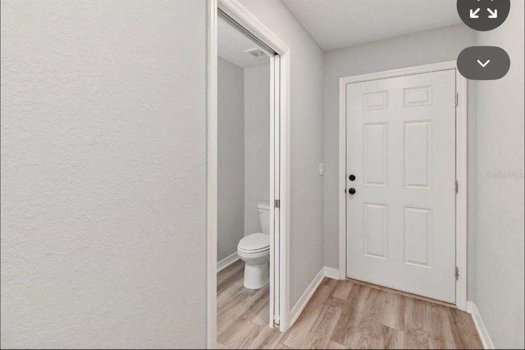 A view of a hallway with light wood-look flooring, a white door, and a bathroom entrance — 2917 FIELDWOOD CIRCLE, ST CLOUD, FL