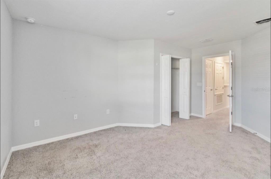An empty bedroom with light gray walls, beige carpet, a closet, and an open doorway — 2917 FIELDWOOD CIRCLE, ST CLOUD, FL