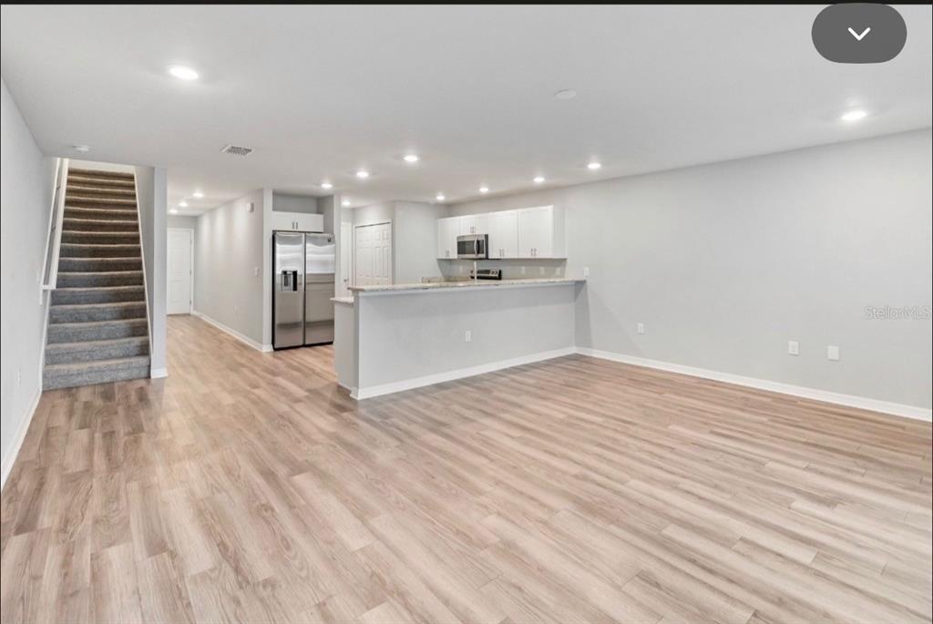 An open-concept living area features light wood-look flooring, a kitchen with white cabinets, and stairs — 2917 FIELDWOOD CIRCLE, ST CLOUD, FL