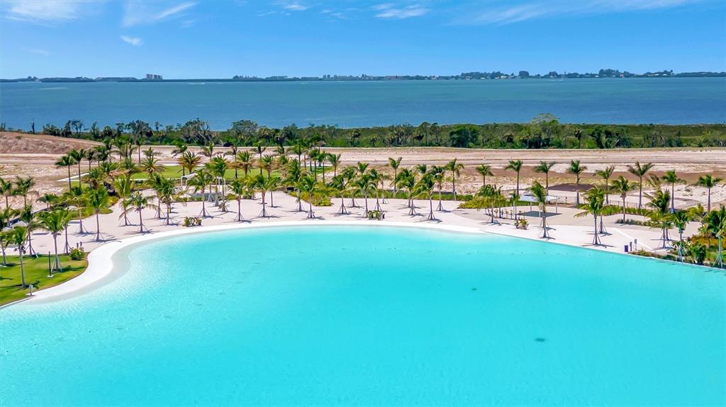 An aerial view shows a large turquoise swimming lagoon surrounded by palm trees and sand — 6027 SALT GRASS STREET, BRADENTON, FL