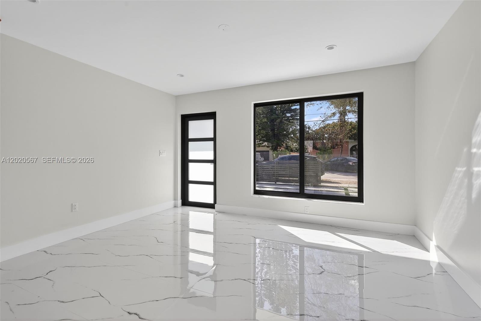 A bright, empty room features white walls, a black-framed door, and polished marble flooring — 53 NW 68th St # 0, Miami FL 33150, MIAMI, FL