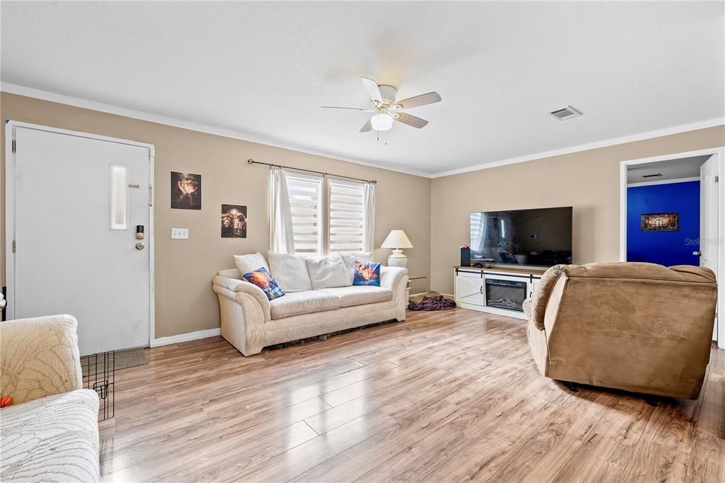 A living room features light wood-look flooring, a white sofa, and a television console — 12275 CROSS STREET, LARGO, FL