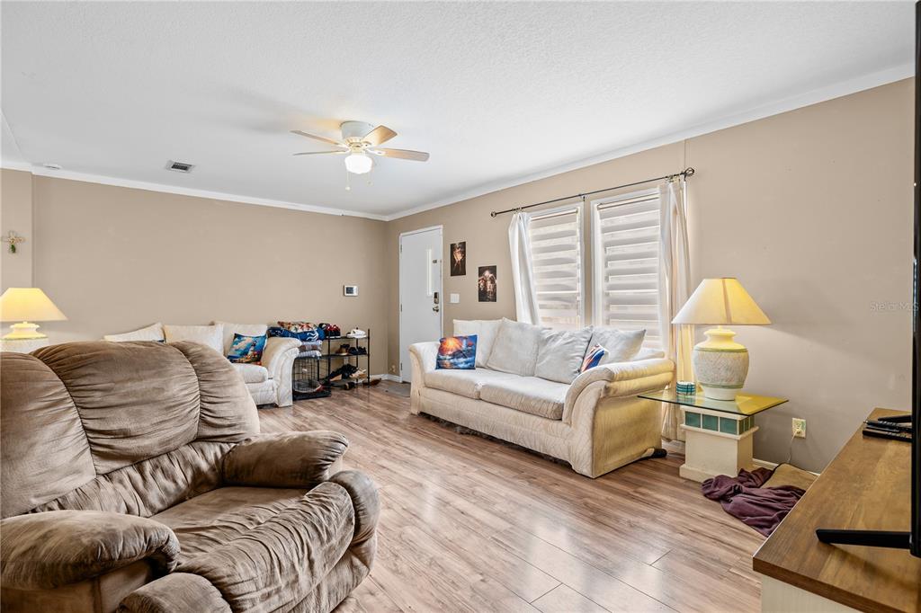 A living room features light wood-look flooring, beige walls, two sofas, and a ceiling fan — 12275 CROSS STREET, LARGO, FL