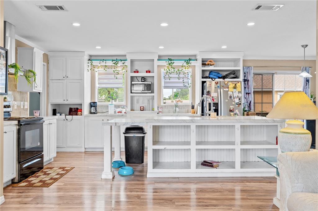 A bright kitchen features white cabinetry, a large marble-topped island, and light wood flooring — 12275 CROSS STREET, LARGO, FL