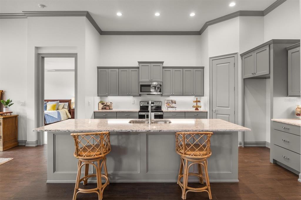 A kitchen features gray cabinets, a large island with two rattan stools, and granite countertops — 7911 LAKE JAMES BOULEVARD, LAKELAND, FL