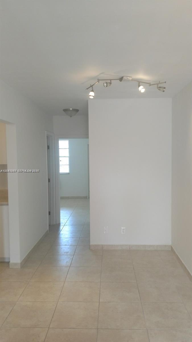 A hallway with tile flooring leads to a room with a window and track lighting — HOLLYWOOD, FL