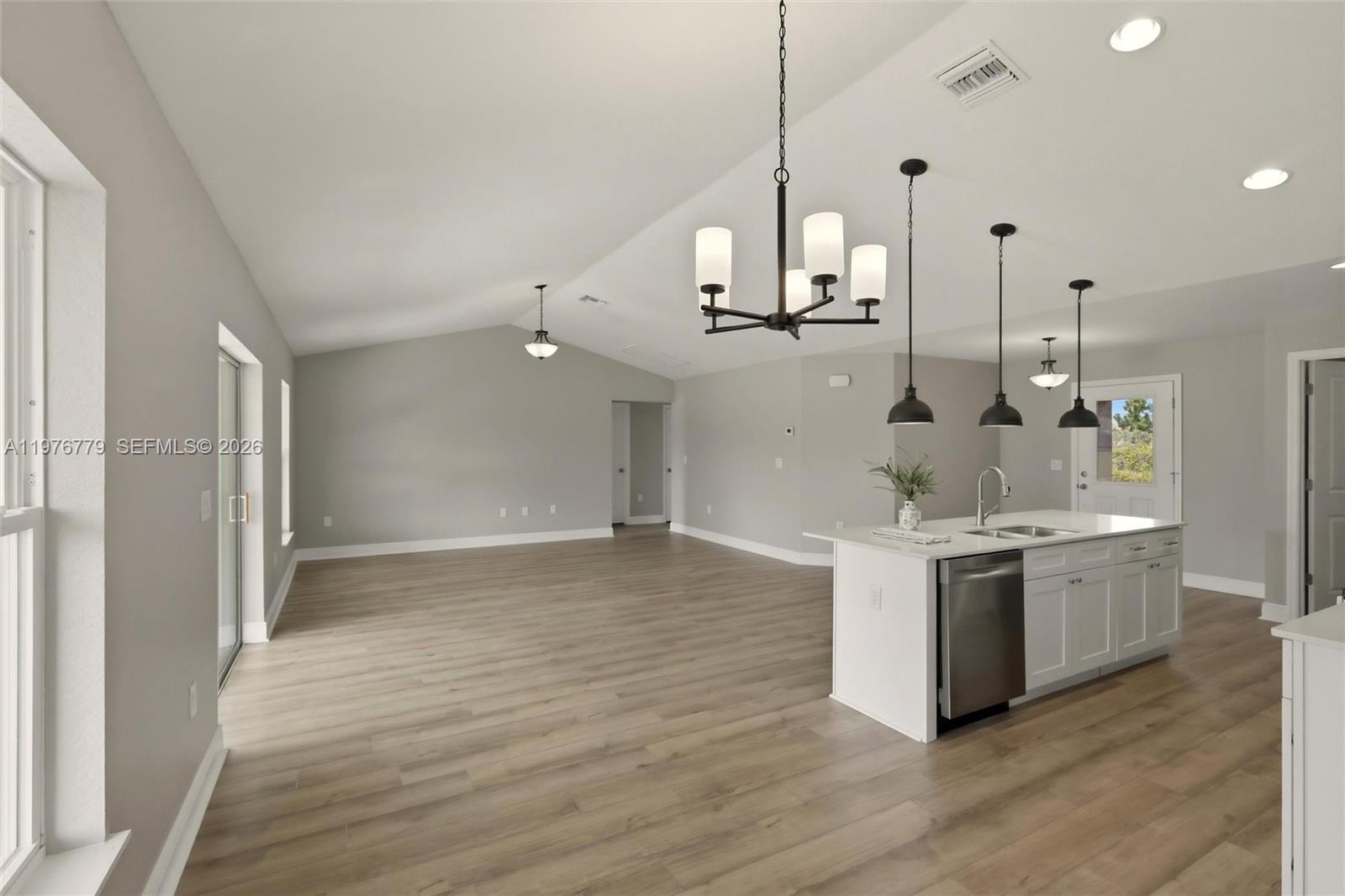 An open-concept kitchen and living area features light wood flooring, white cabinets, and vaulted ceilings — 6809 Dickinson Drive, Sebring FL 33872, SEBRING, FL