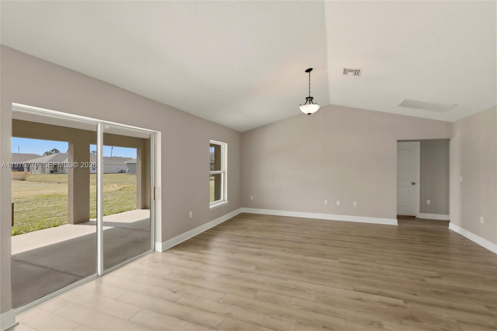An empty living room features light wood-look flooring, beige walls, a vaulted ceiling, and sliding doors — 6809 Dickinson Drive, Sebring FL 33872, SEBRING, FL
