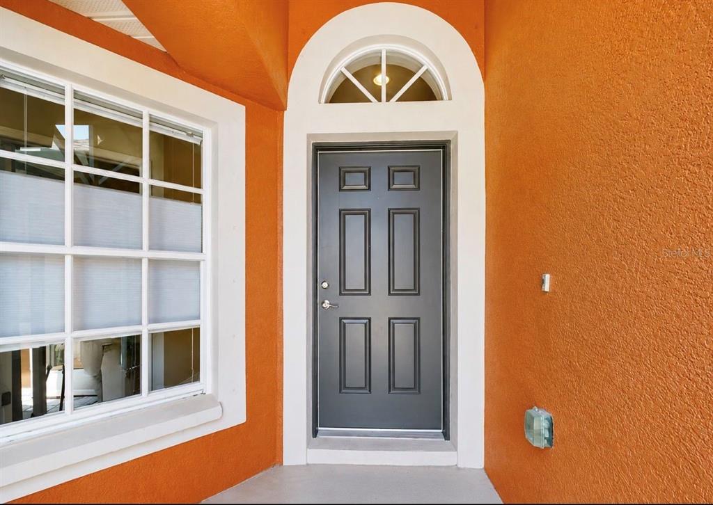 A dark gray front door with a transom window is set in an orange stucco wall — 1836 RAVEN GLEN DRIVE, RUSKIN, FL