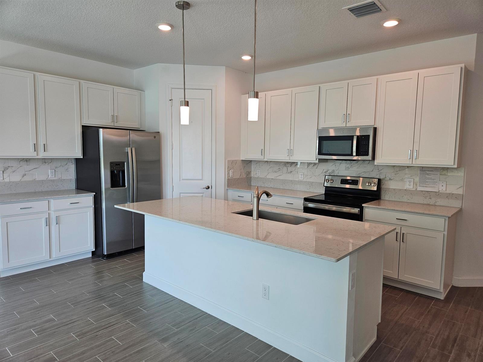 A modern kitchen features white cabinets, stainless steel appliances, a center island, and tile flooring — 15018 Three Ponds Trail, Delray Beach FL 33446, DELRAY BEACH, FL