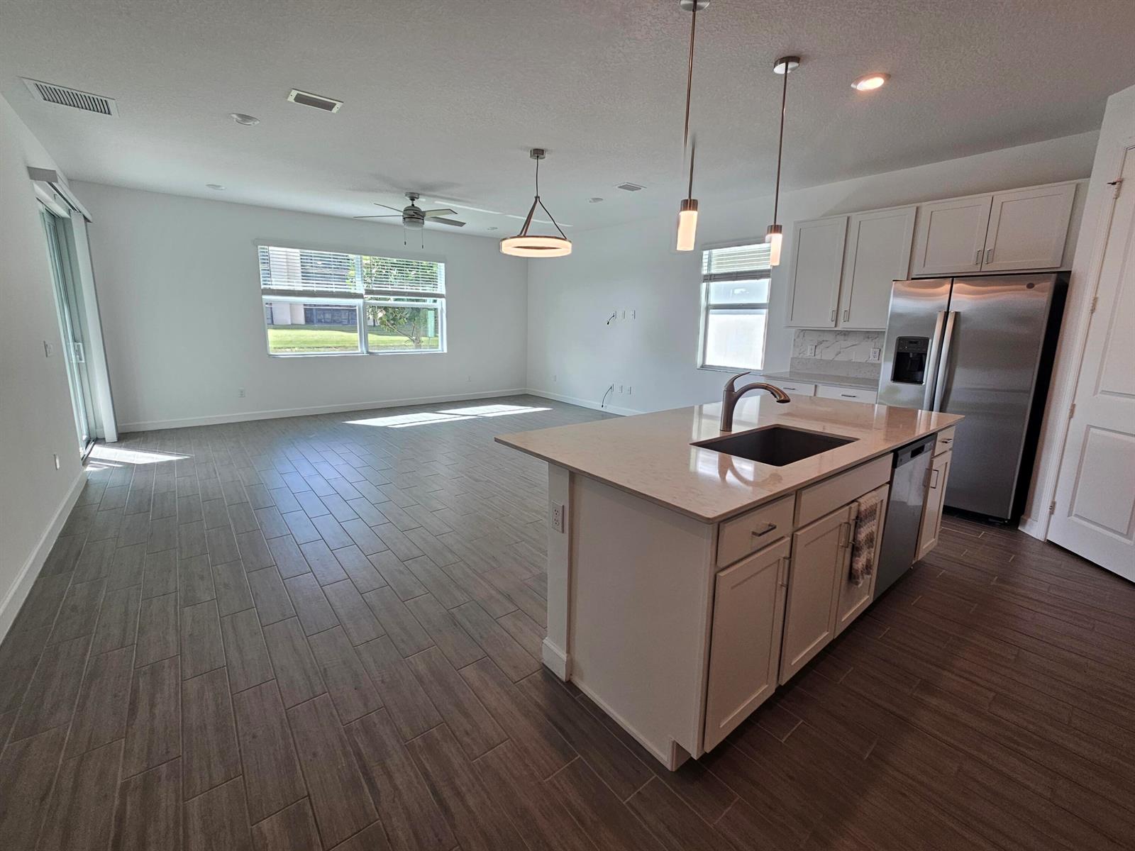 An open-concept kitchen and living area features light cabinetry, a central island, and tile flooring — 15018 Three Ponds Trail, Delray Beach FL 33446, DELRAY BEACH, FL