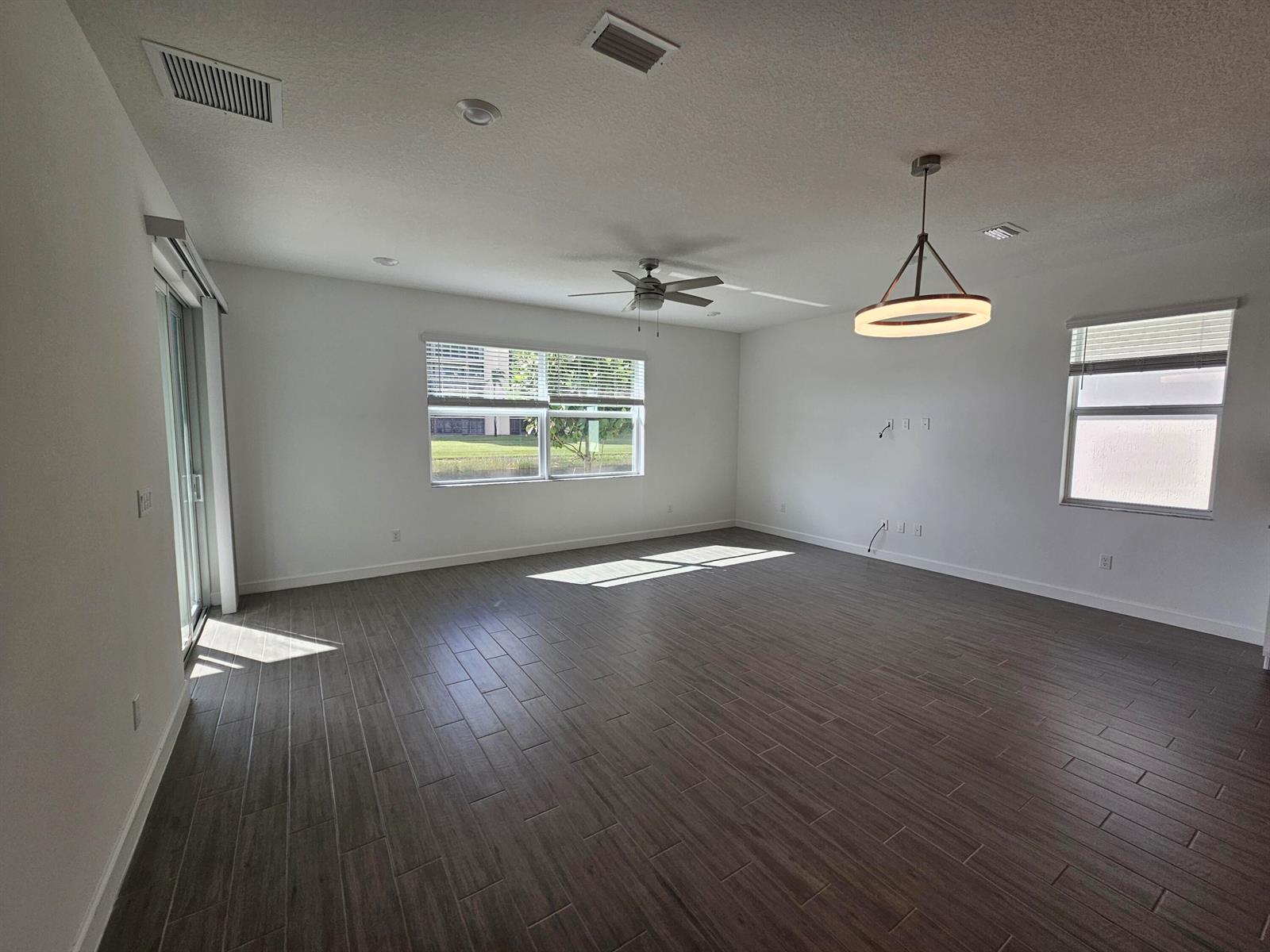 An empty living room features white walls, dark wood-look tile flooring, and a modern chandelier — 15018 Three Ponds Trail, Delray Beach FL 33446, DELRAY BEACH, FL