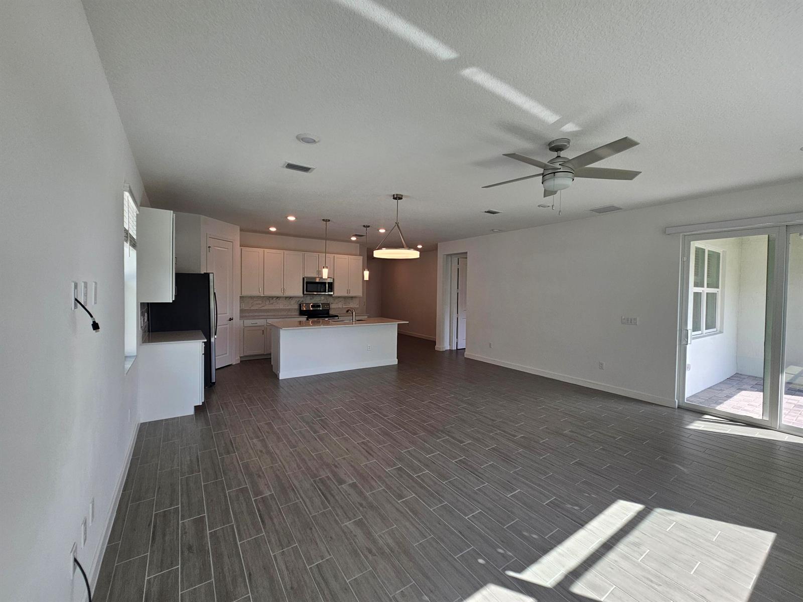 An open-concept kitchen and living area features white cabinetry, a center island, and gray flooring — 15018 Three Ponds Trail, Delray Beach FL 33446, DELRAY BEACH, FL