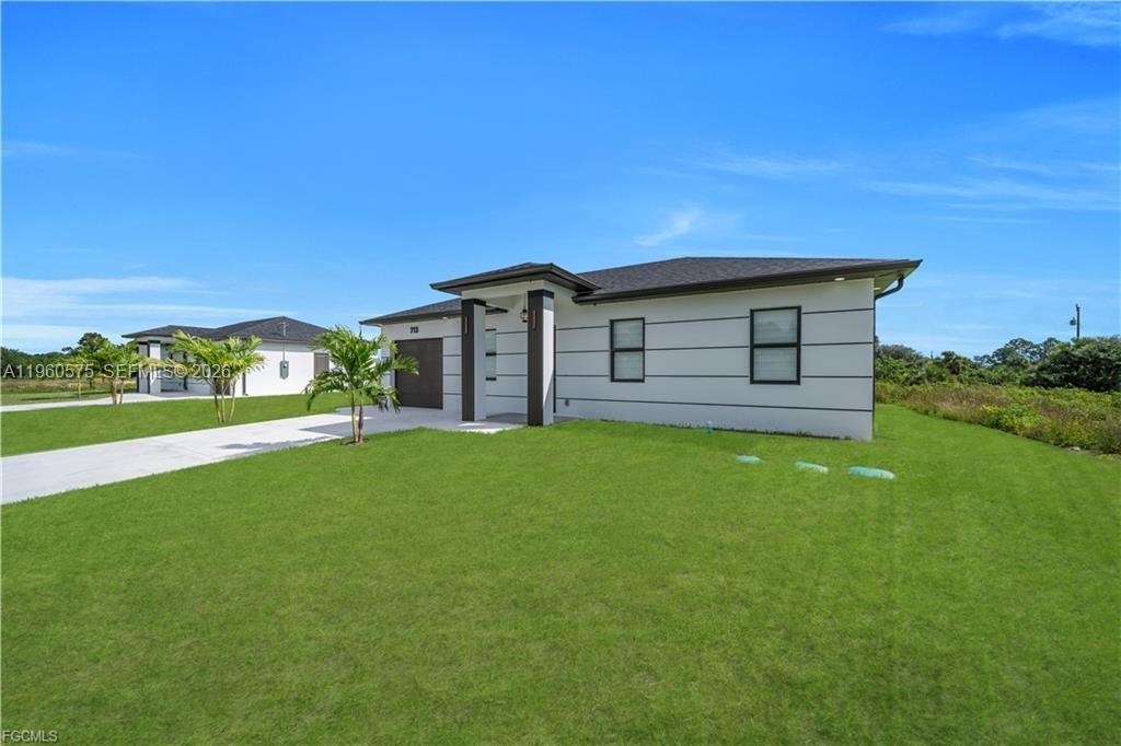 A modern, single-story white house with a dark roof stands on a grassy lot — 711 Roma Ave, Lehigh Acres FL 33974, LEHIGH ACRES, FL