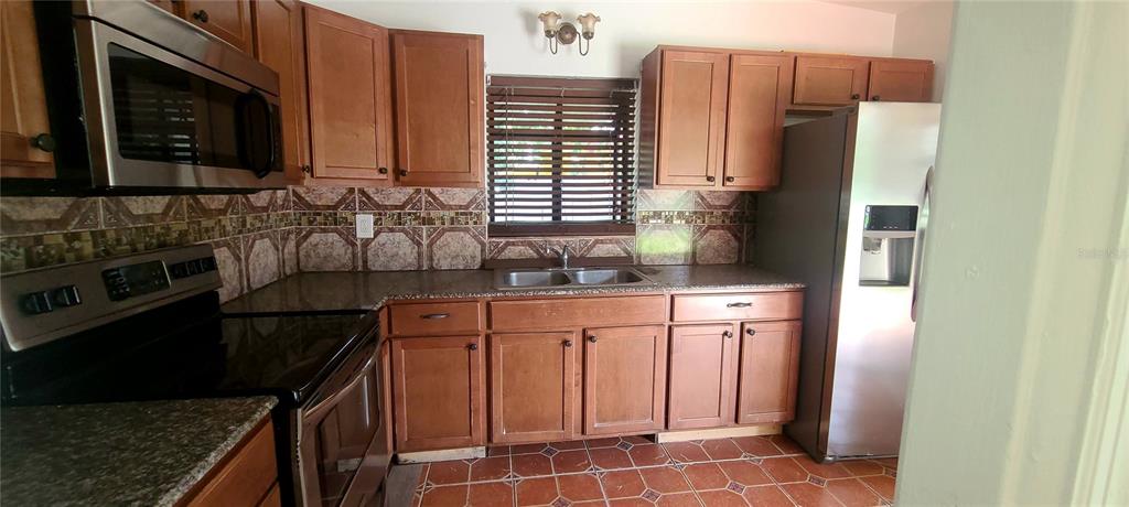 A kitchen features wood cabinets, granite countertops, a stainless steel microwave, and tiled flooring — 301 HOPE CIRCLE, ORLANDO, FL