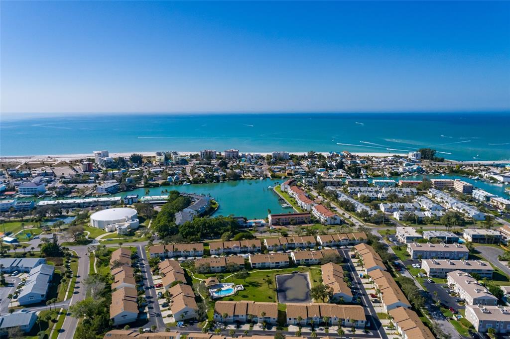 An aerial view shows a coastal residential community with townhomes, a pool, and a lagoon — 216 SUN VISTA CT S, TREASURE ISLAND, FL