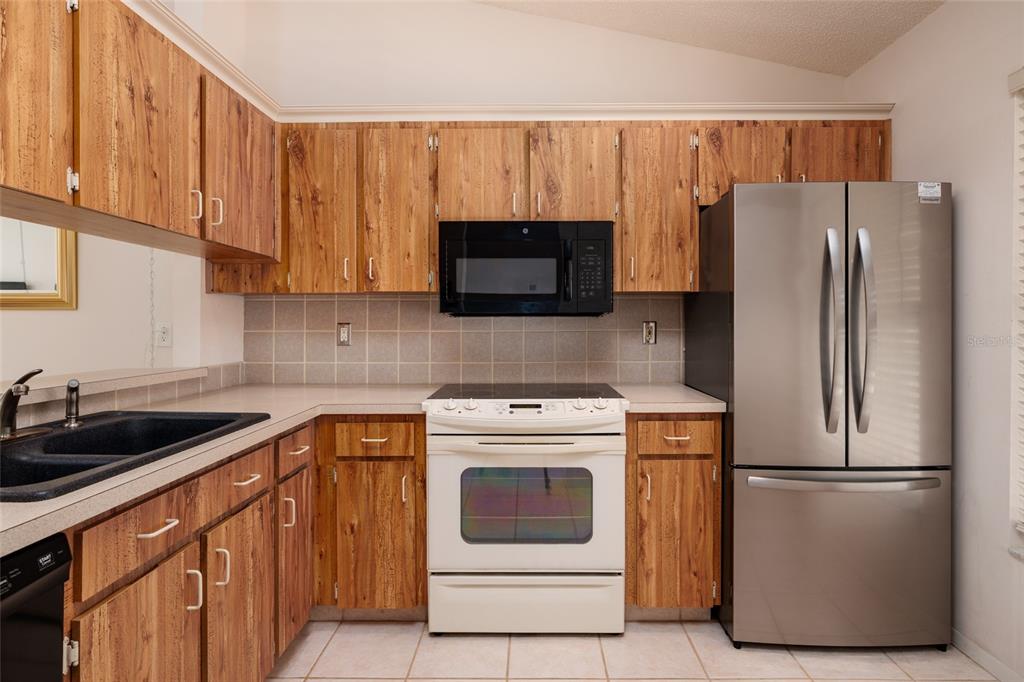 A kitchen featuring wood-grain cabinets, a white stove, a black microwave, and a stainless refrigerator — 216 SUN VISTA CT S, TREASURE ISLAND, FL