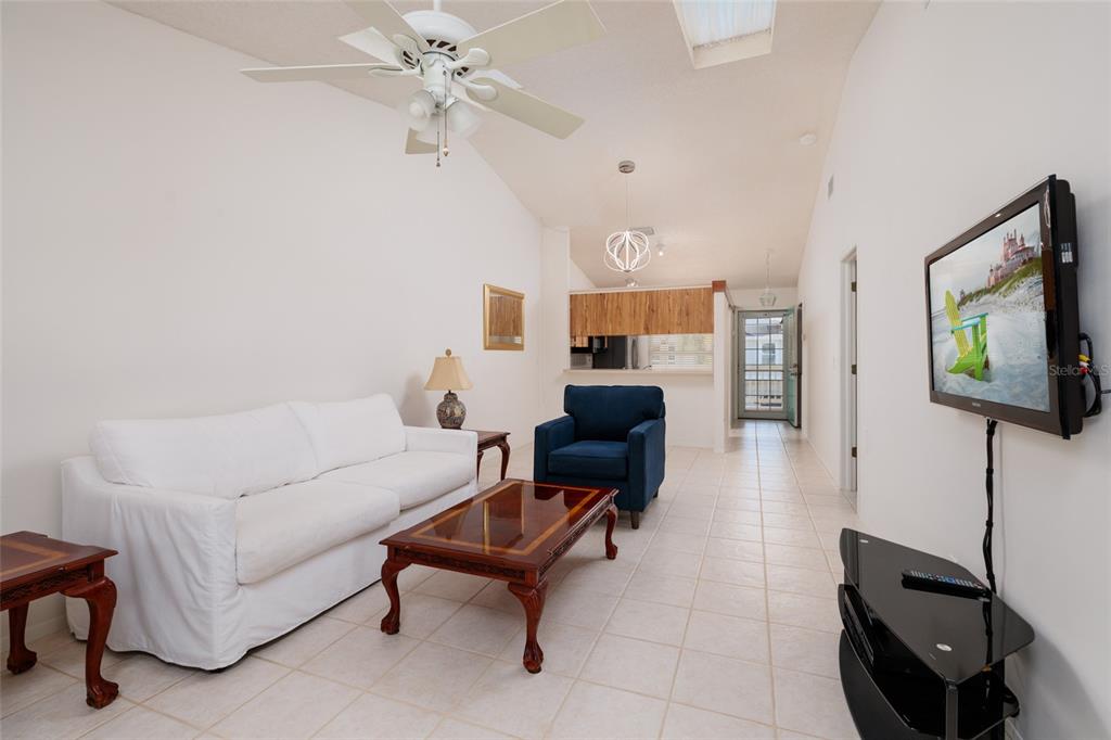 A living room features a white sofa, blue armchair, coffee table, and a wall-mounted television — 216 SUN VISTA CT S, TREASURE ISLAND, FL