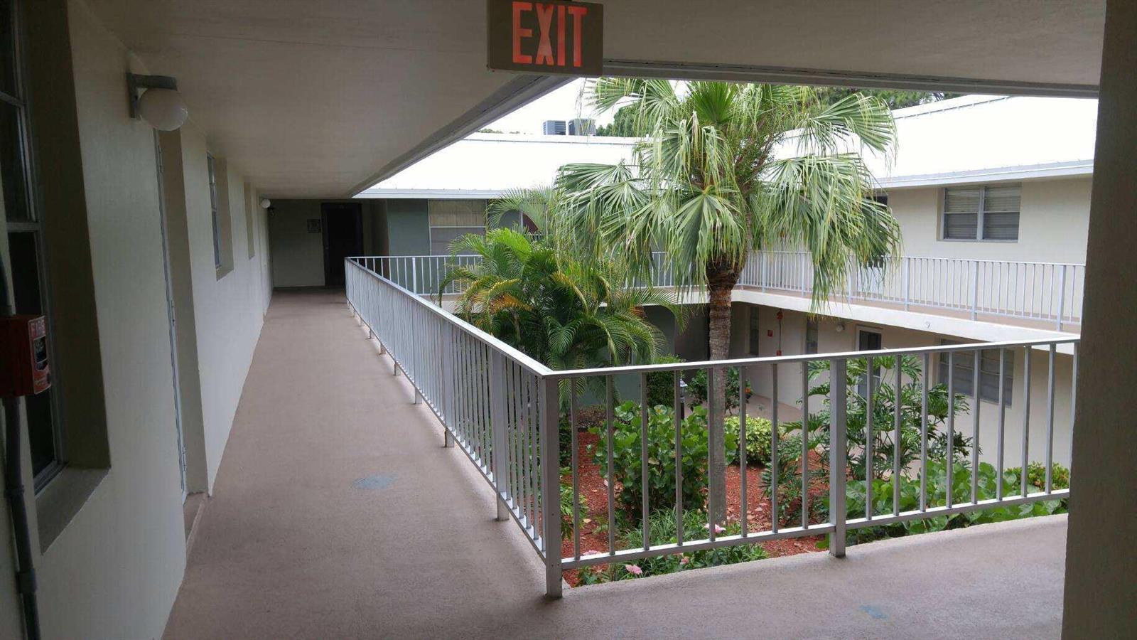 An outdoor apartment building walkway overlooks a central courtyard with a palm tree and plants — 2302 Sunrise Boulevard # 201, Fort Pierce FL 34982, FORT PIERCE, FL