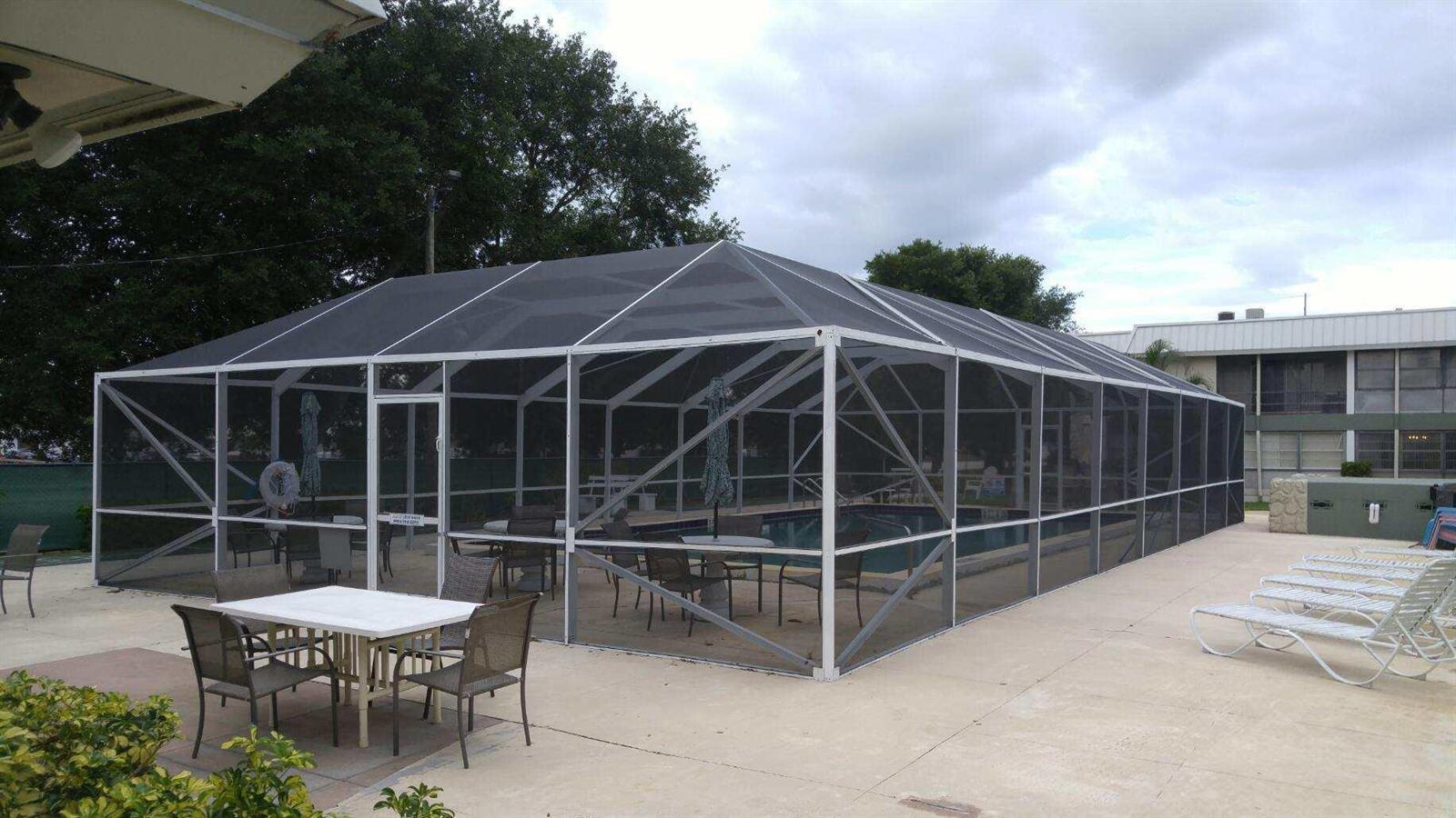 A large rectangular swimming pool is enclosed by a white-framed screen structure on a patio — 2302 Sunrise Boulevard # 201, Fort Pierce FL 34982, FORT PIERCE, FL