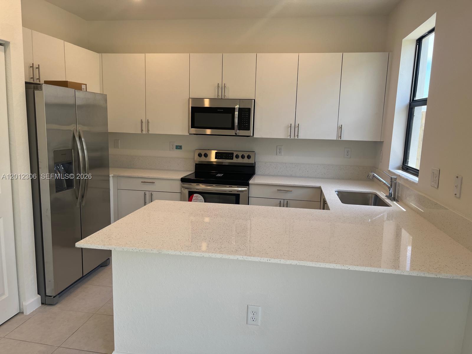 A modern kitchen features white cabinets, stainless steel appliances, and light-colored speckled countertops — 12912 SW 233rd Ter, Homestead FL 33032, HOMESTEAD, FL