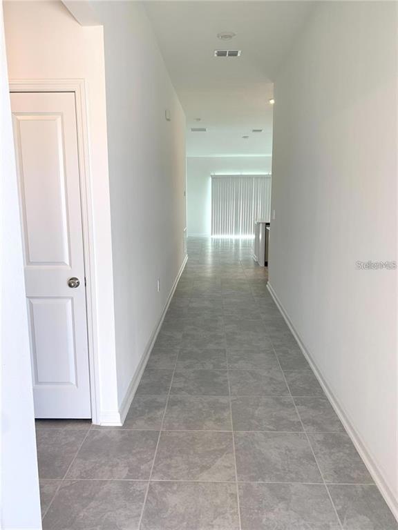 A hallway with gray tile flooring leads toward a bright room with vertical blinds — 1373 BRENTWOOD DR, KISSIMMEE, FL