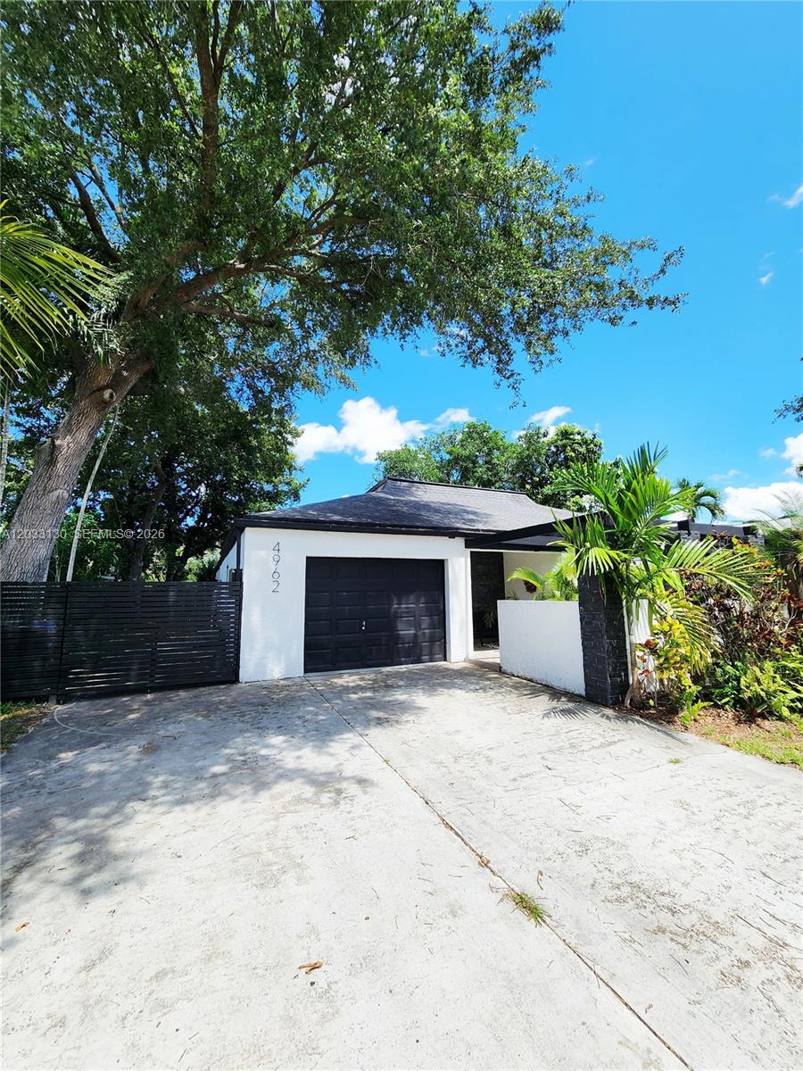 A single-story house with a black garage door, white walls, and a large tree — 4962 SW 95th Ave, Cooper City FL 33328, COOPER CITY, FL