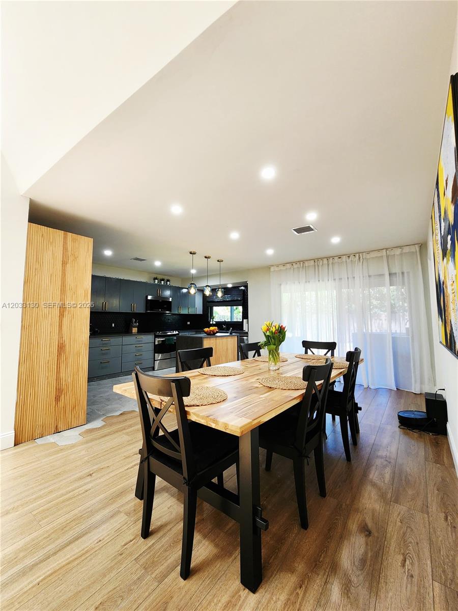 A dining room with a wooden table and black chairs sits adjacent to a kitchen — 4962 SW 95th Ave, Cooper City FL 33328, COOPER CITY, FL