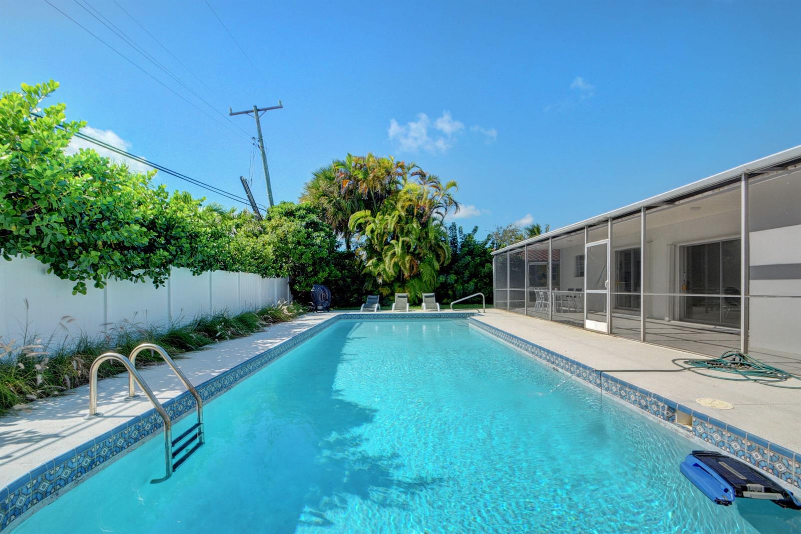 A rectangular swimming pool with a metal ladder sits beside a screened-in patio and fence — 1171 Bimini Lane, Singer Island FL 33404, SINGER ISLAND, FL