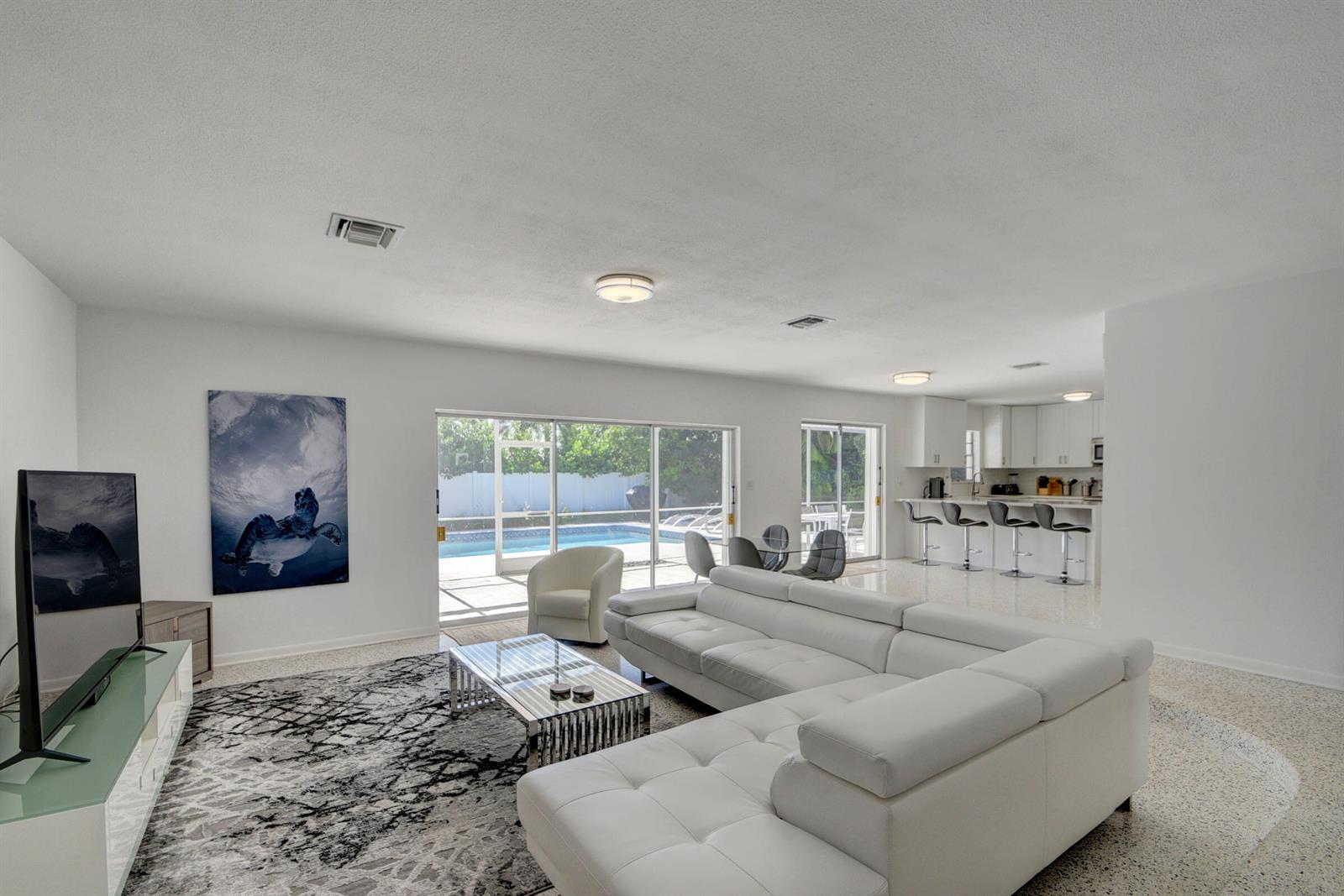 A modern living room with a white sectional sofa, patterned rug, and sliding doors to a pool — 1171 Bimini Lane, Singer Island FL 33404, SINGER ISLAND, FL