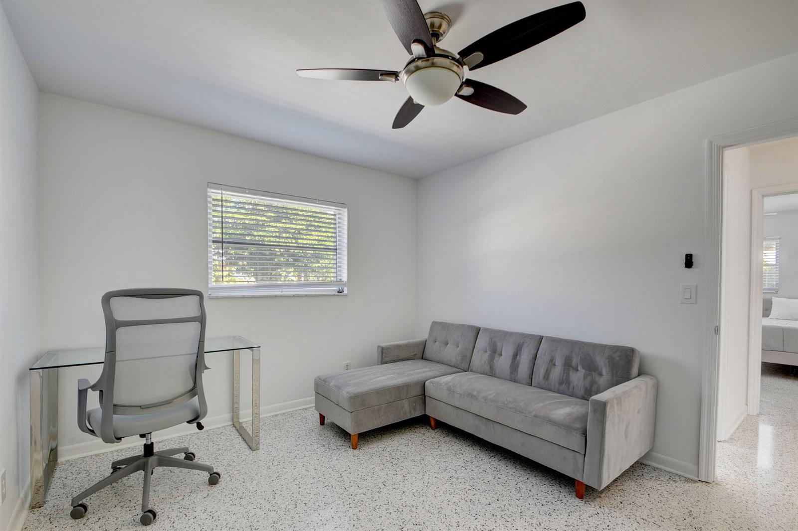 A home office with a glass desk, grey sofa, ceiling fan, and speckled flooring — 1171 Bimini Lane, Singer Island FL 33404, SINGER ISLAND, FL
