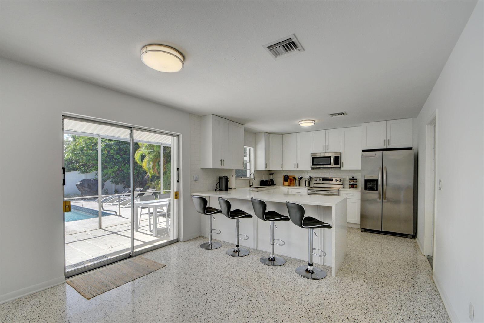 A modern kitchen features white cabinetry, stainless steel appliances, a breakfast bar, and terrazzo flooring — 1171 Bimini Lane, Singer Island FL 33404, SINGER ISLAND, FL