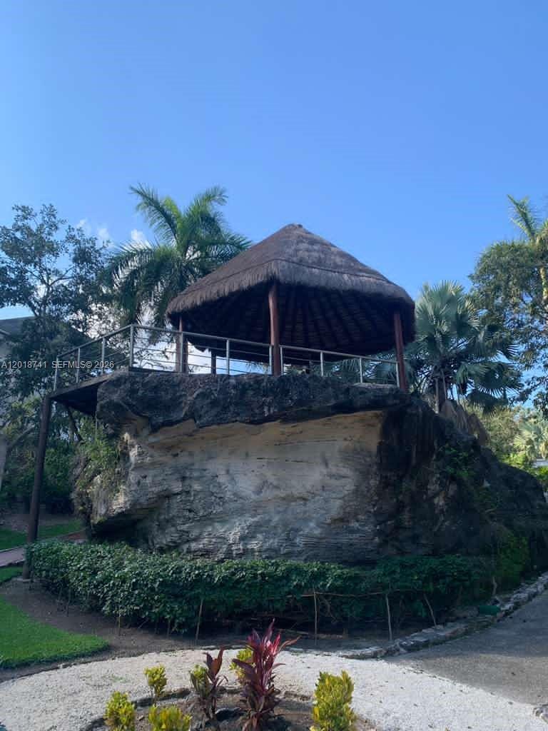 A thatched-roof gazebo sits atop a large natural rock formation in a landscaped garden — MZ10 L25 Calle Isla, TX 77586, TX