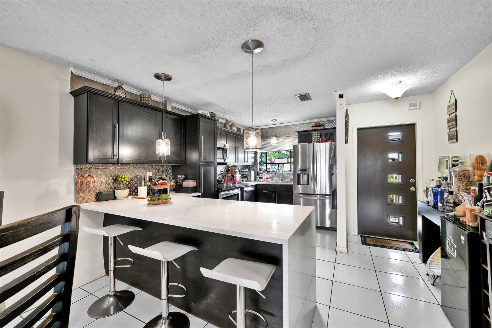A kitchen features dark cabinetry, a white quartz island with three stools, and tile flooring — 627 Banks Road # 48, Margate FL 33063, MARGATE, FL