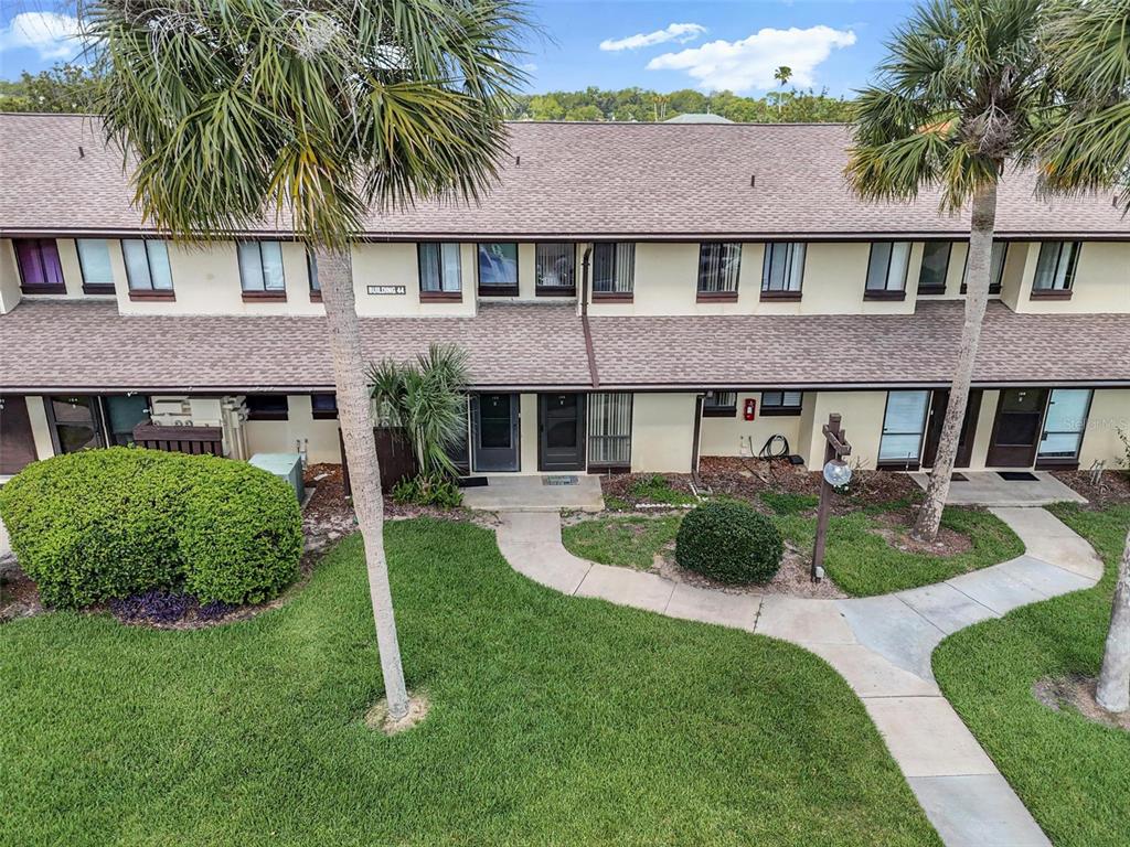 A two-story residential building with a tan facade, brown shingled roof, and palm trees — 44 CLUB HOUSE DRIVE UNIT 106, PALM COAST, FL
