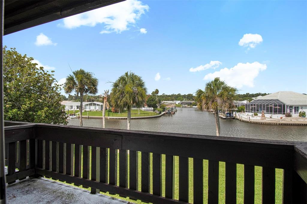 A balcony with a dark wooden railing overlooks a canal surrounded by houses and trees — 44 CLUB HOUSE DRIVE UNIT 106, PALM COAST, FL