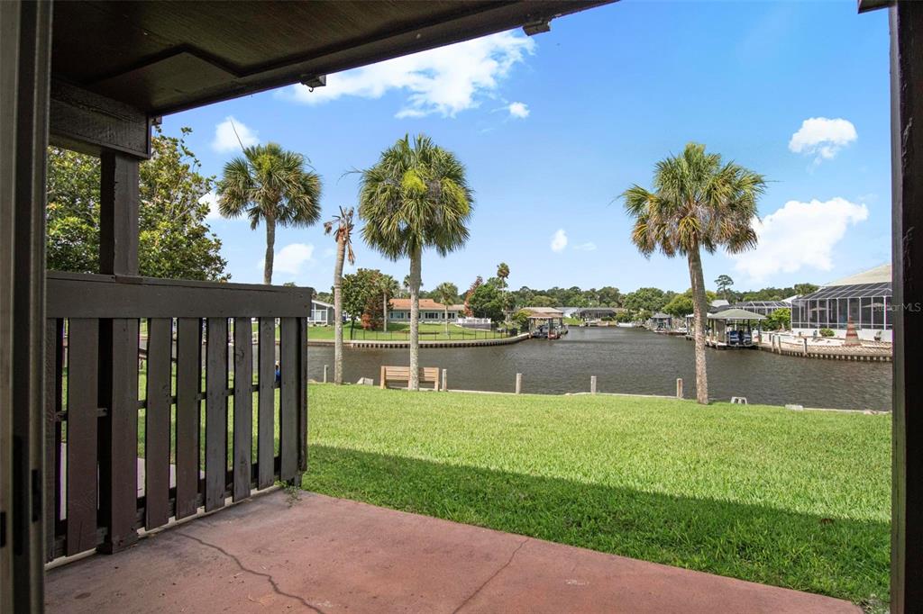 A view from a covered patio looking out over a grassy lawn toward a canal — 44 CLUB HOUSE DRIVE UNIT 106, PALM COAST, FL
