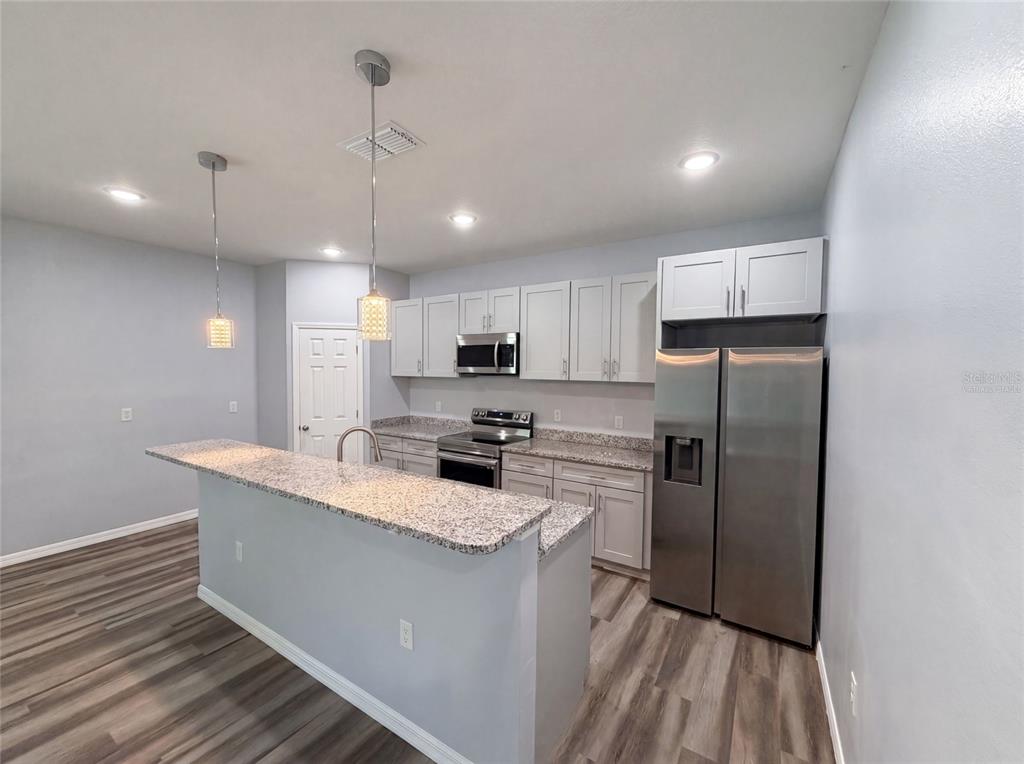 A kitchen features white cabinets, granite countertops, stainless steel appliances, and wood-look flooring — 1013 W 11TH STREET, SANFORD, FL