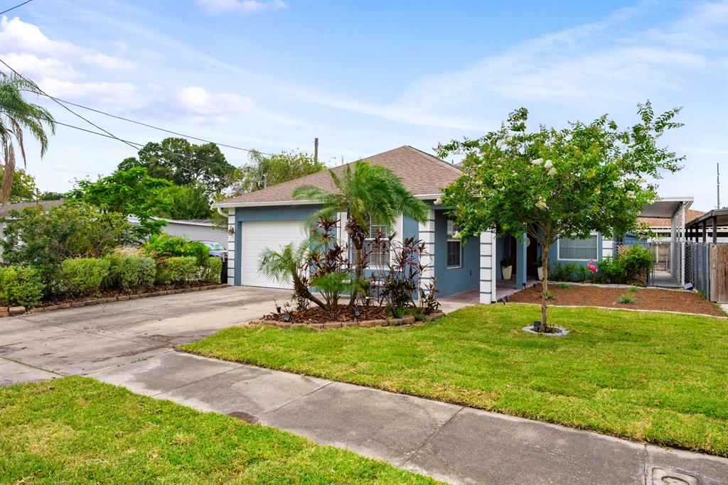 A blue single-story house features a white garage door, a front lawn, and landscaping — 3411 W NORTH B STREET, TAMPA, FL