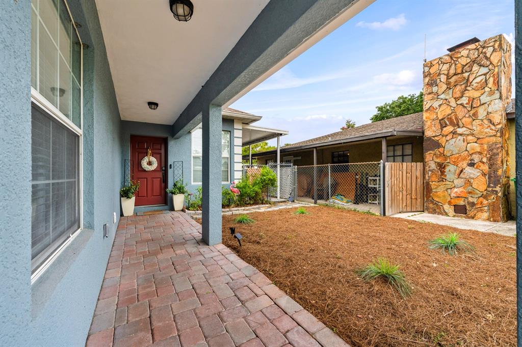 A covered brick walkway leads to a red front door beside a stone chimney exterior — 3411 W NORTH B STREET, TAMPA, FL