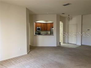 A carpeted living area looks through an arched opening into a kitchen with wood cabinets — 3301 WHITESTONE CIRCLE UNIT 205, KISSIMMEE, FL