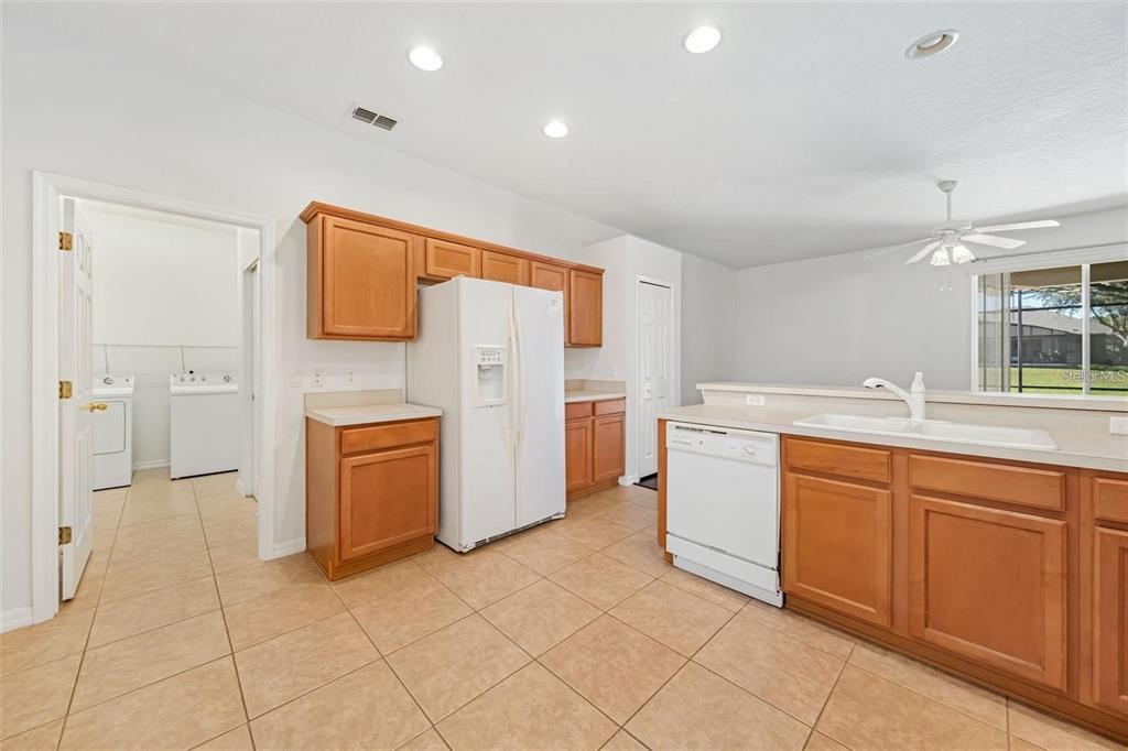 A kitchen with wood cabinets, white appliances, and tile flooring, featuring an adjacent laundry room — 9651 OLD MARSH COURT, ORLANDO, FL